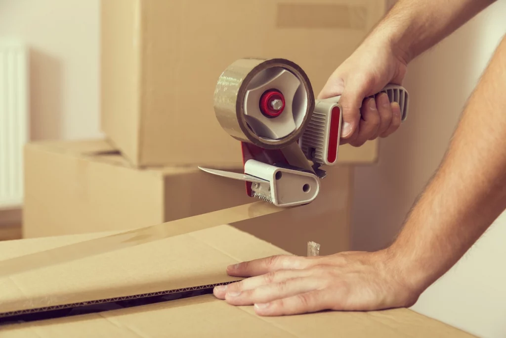 picture of a person using a packing tape gun to seal a cardboard box with tape